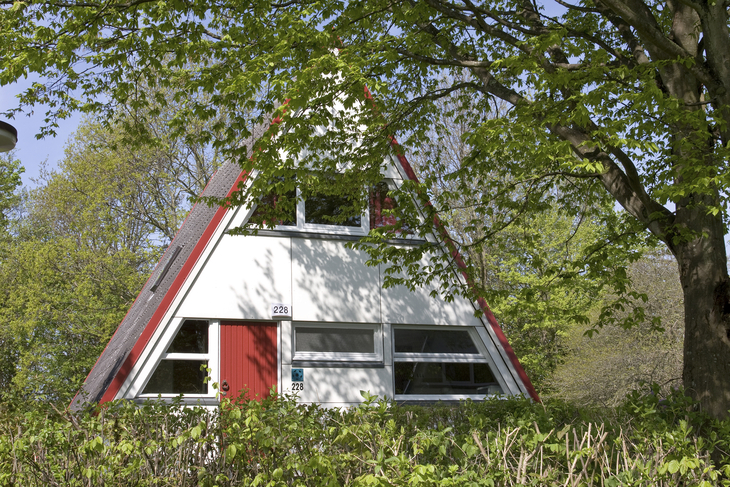 Nurdachhaus im Grünen mit Bäumen im Hintergrund.