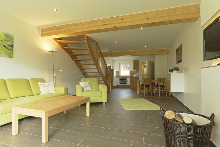 Modernes Wohnzimmer mit grünen Sofas, Holzmöbeln und Treppe in einem Ferienhaus.