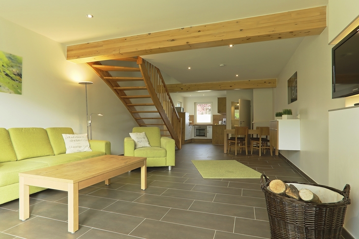 Wohnzimmer eines Ferienhauses mit grüner Couch und Holztreppe zur oberen Etage.