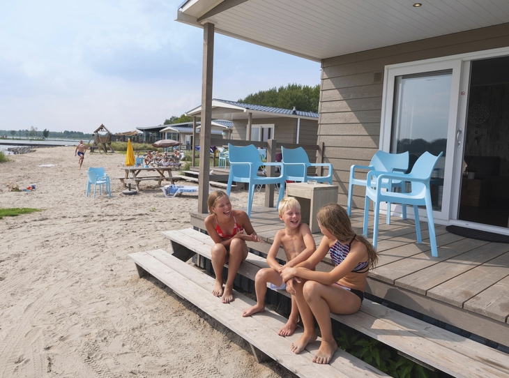 Drei Kinder sitzen auf einer Veranda am Strand neben Ferienhäusern.