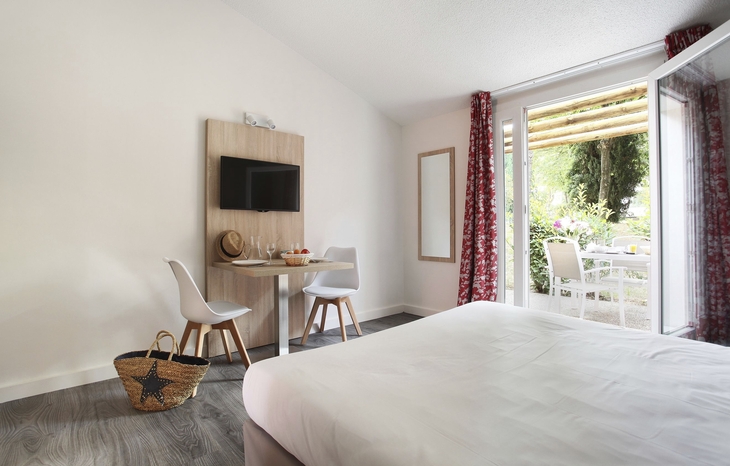 Helles Hotelzimmer mit Bett, Tisch, Stühlen und offenem Zugang zur Terrasse.