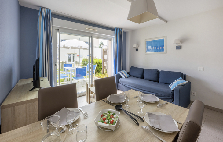 Essbereich und Wohnzimmer einer modernen Ferienwohnung mit gedecktem Tisch und Balkonblick.