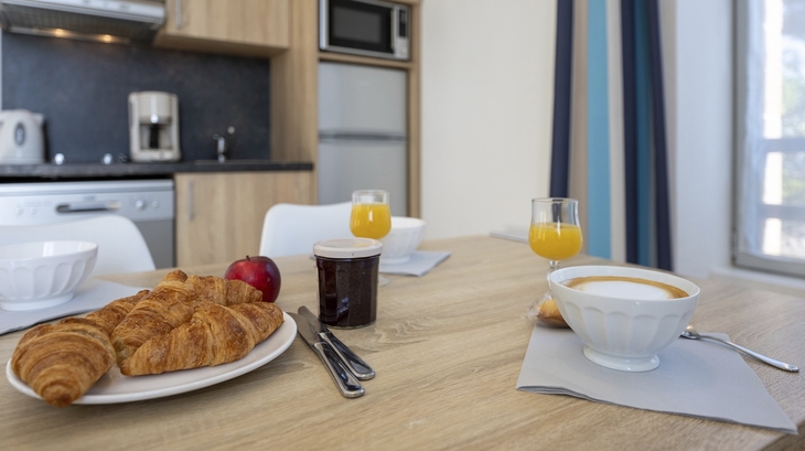 Frühstückstisch mit Croissants, Marmelade und Orangensaft in moderner Küche.
