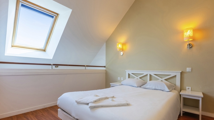Helles Schlafzimmer mit Doppelbett, Dachfenster und Nachttischen.