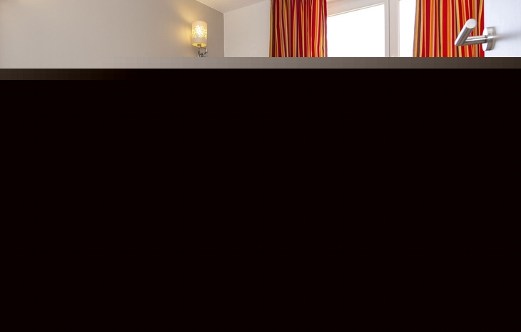 Schlafzimmer mit Doppelbett, farbiger Bettdecke und Fenster mit gestreiften Vorhängen.