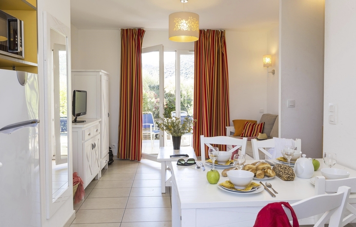 Helles Wohnzimmer mit Esstisch, gedeckt für Frühstück, und Balkonzugang.