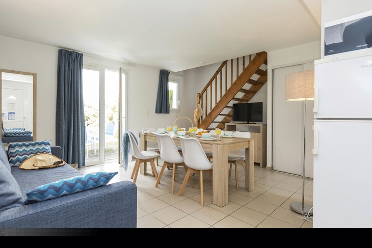 Wohnzimmer mit Esstisch, Sofa, Treppe und Glastüren in einem Ferienhaus.