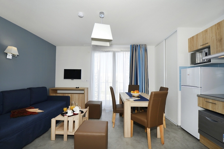 Wohnzimmer mit Esstisch, blauer Couch und Fernseher in moderner Ferienwohnung.