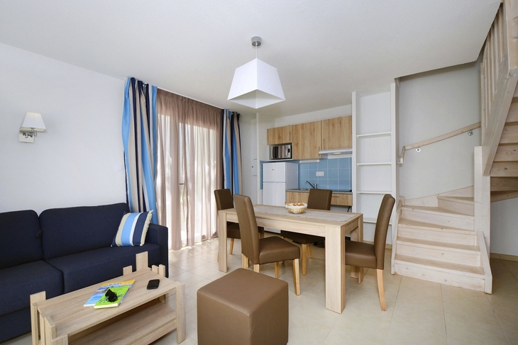 Helles Wohnzimmer mit Esstisch, Stühlen, Sofa und Treppe in einem Apartment.
