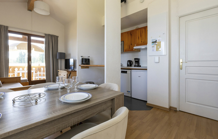 Essbereich mit Holz-Tisch, gedeckt mit Geschirr, offene kleine Küche im Hintergrund.