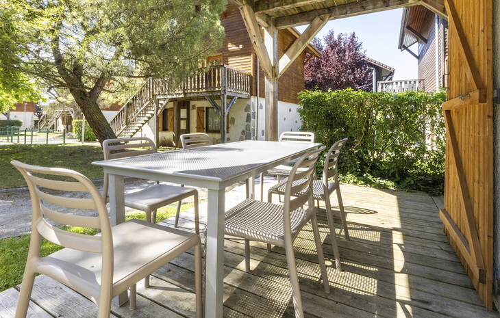 Terrasse mit Tisch und Stühlen, umgeben von Bäumen in einer Chalet-Anlage.