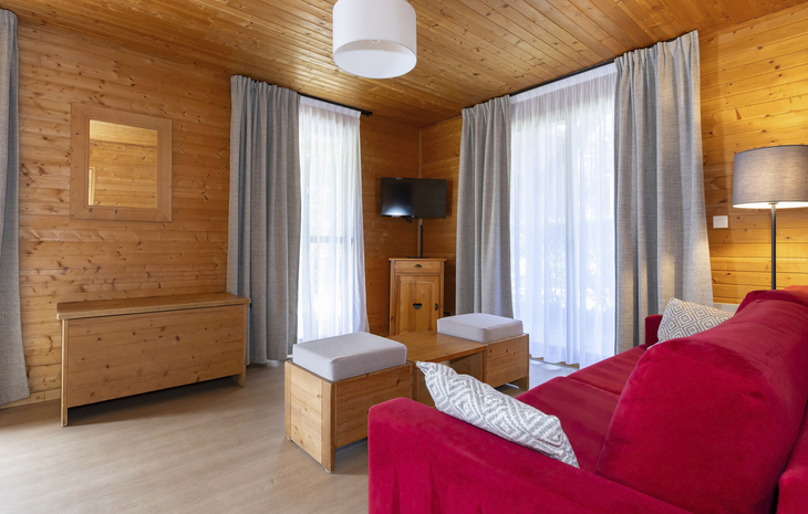 Holzvertäfeltes Wohnzimmer mit rotem Sofa, Fernseher und großen Fenstern