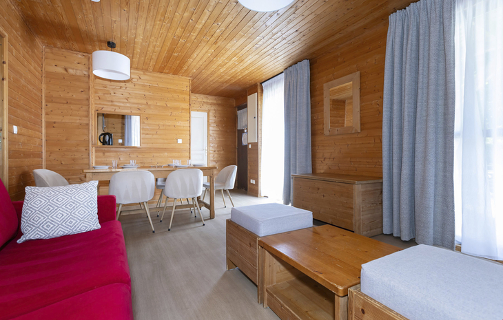 Gemütliches Wohnzimmer in Holzoptik mit Esstisch und roten Akzenten.
