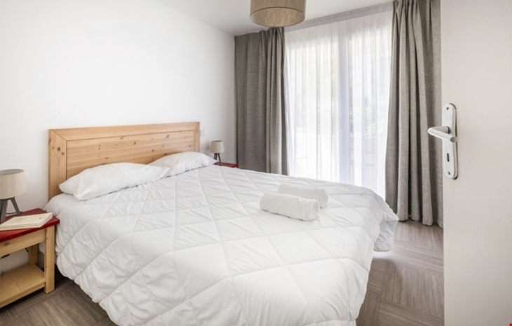 Helles Schlafzimmer mit Doppelbett und großen Fenstern in einer Ferienwohnung.