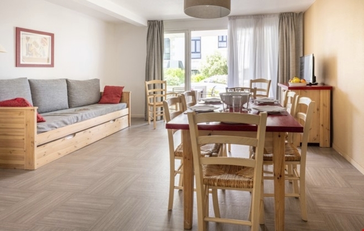 Wohnzimmer mit Esstisch, Stühlen, Sofa und Fernseher in heller Ferienwohnung.