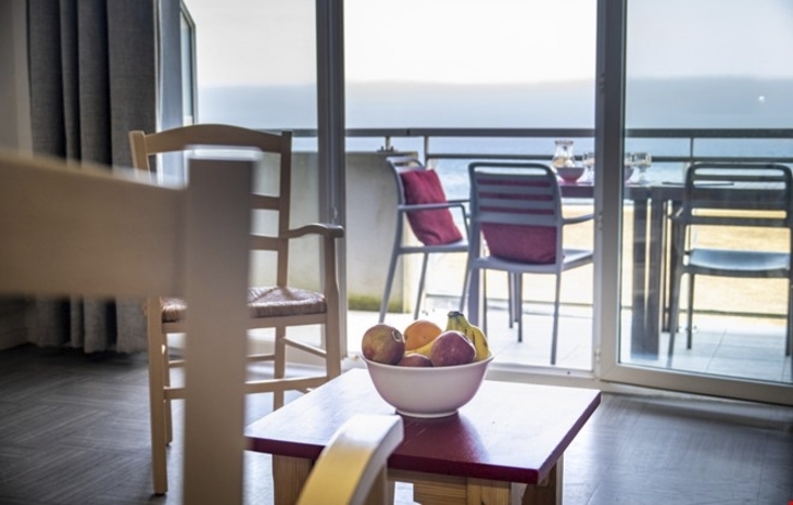 Blick von einem Wohnraum auf Balkon mit Meerblick, Schüssel mit Früchten im Vordergrund.
