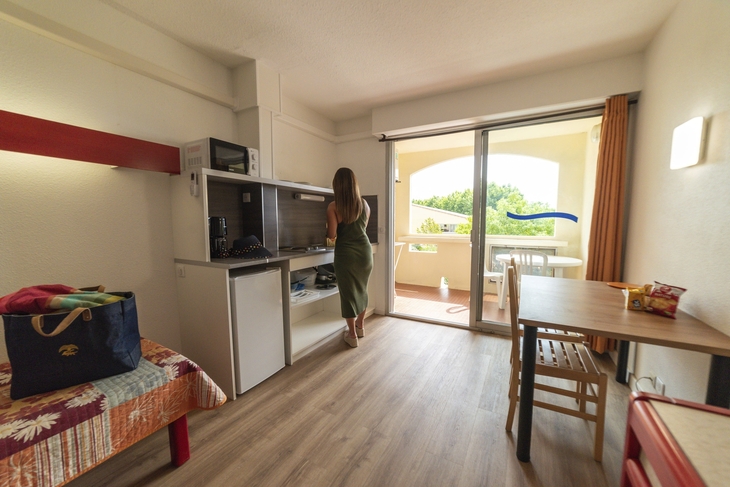 Frau in Studio-Apartment mit Balkon und Küchenzeile.