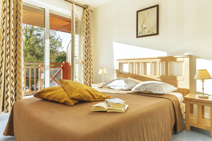 Helles Schlafzimmer mit Doppelbett, zwei Kissen und offenem Balkon.