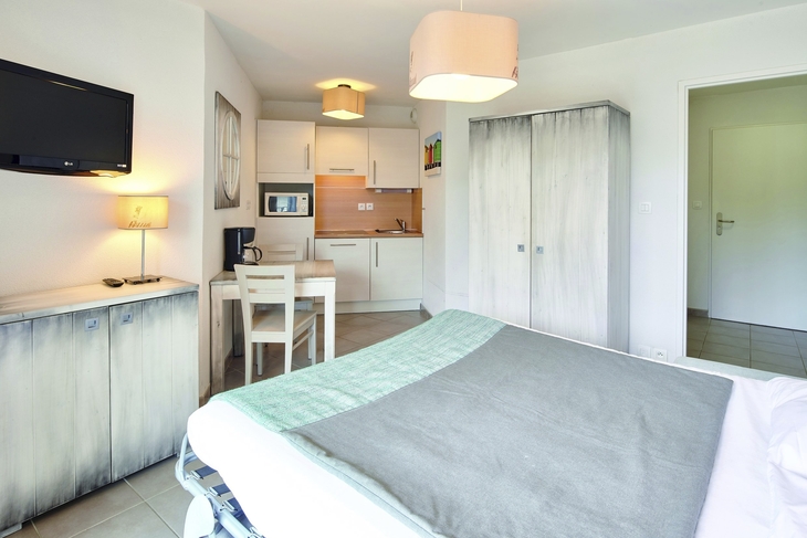 Schlafzimmer mit Bett, Schrank, Schreibtisch und kleinem Küchenbereich.