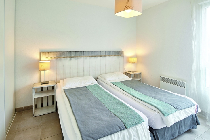 Helles Schlafzimmer mit zwei Einzelbetten, Nachttischen und Lampen.