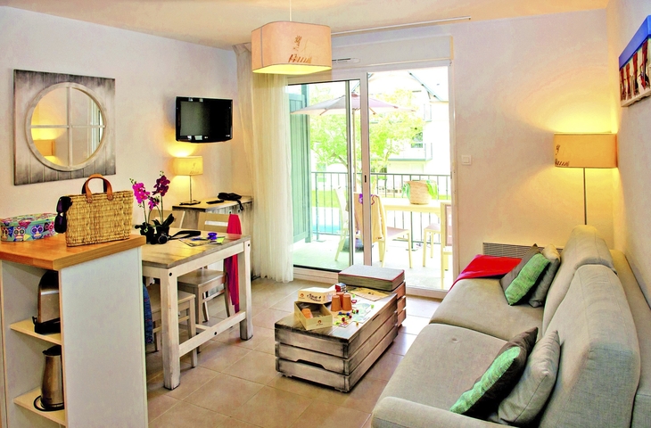 Helles Wohnzimmer mit Sofa, Tisch, TV und Balkonzugang.