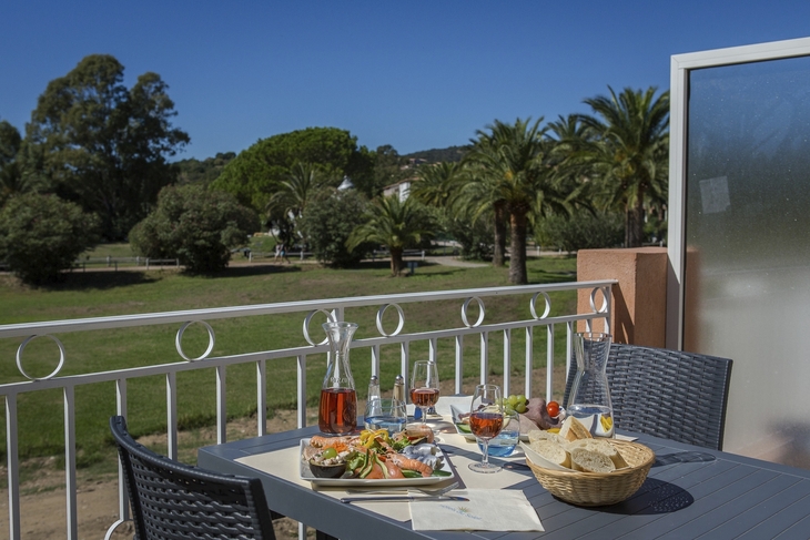 Terrasse mit gedecktem Tisch, Blick auf Garten mit Palmen und Bäumen.