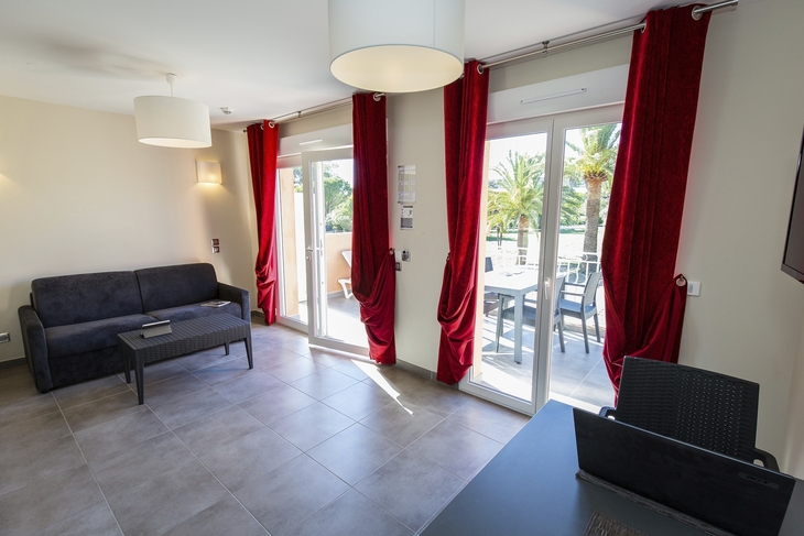 Wohnzimmer mit rotem Vorhang, Sofa und Blick auf Balkon mit Palmen.