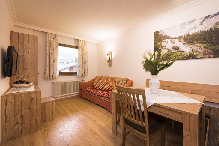 Wohnzimmer mit Holzdekor, Sofa, Tisch und Berglandschaftsbild an der Wand.
