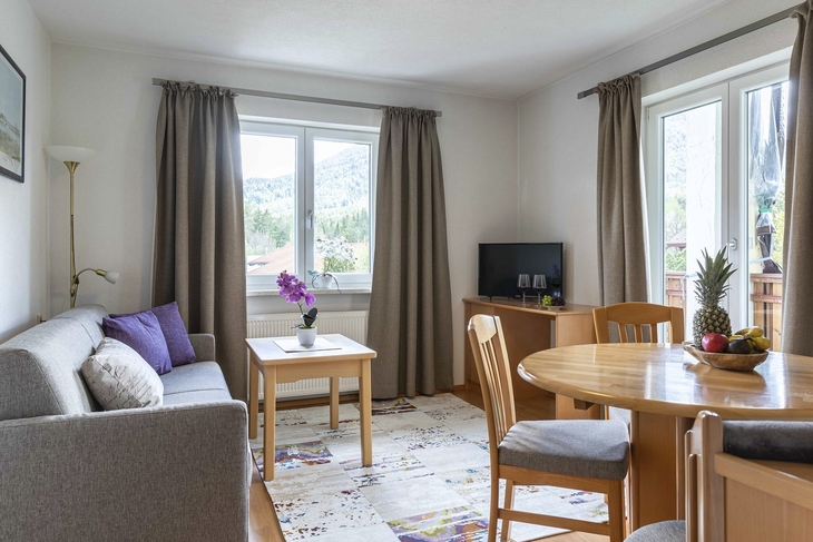 Wohnzimmer mit Sofa, Tisch, Fernseher und Esstisch mit Obstschale.