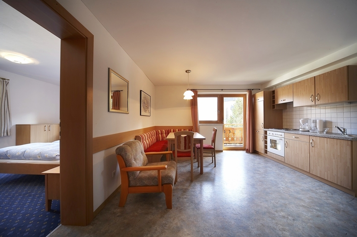 Wohnzimmer mit Küchenzeile, Esstisch und Zugang zu einem Balkon.