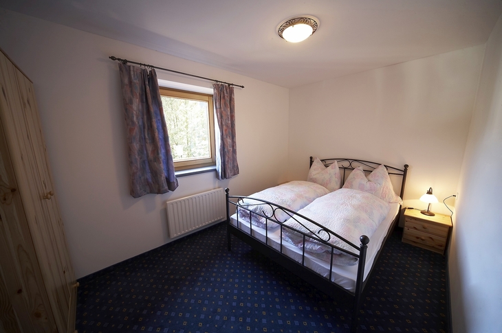 Schlafzimmer mit Doppelbett, Fenster und Nachtischlampe, gemütlich eingerichtet.