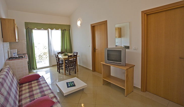 Wohnraum mit Sofa, Esstisch, Fernseher und Balkon im Hintergrund.