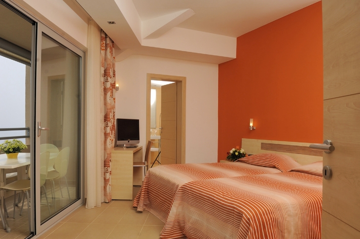 Hotelzimmer mit zwei Betten, orange Akzentwand und Balkonzugang.
