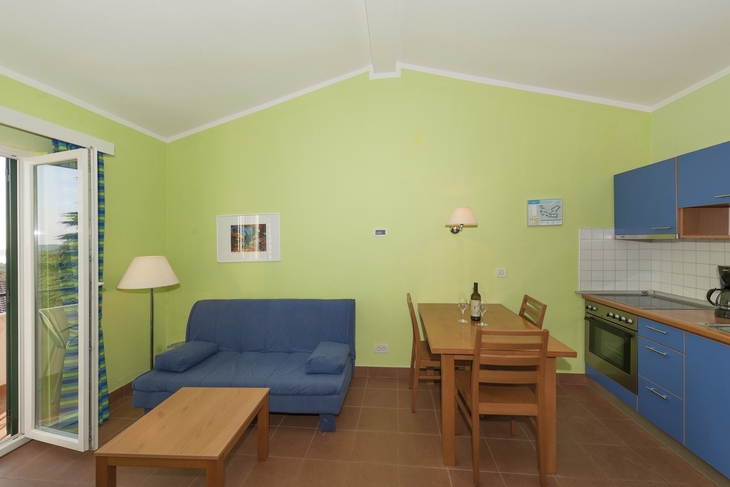 Wohnzimmer mit blauer Couch, Esstisch und offener Küche.