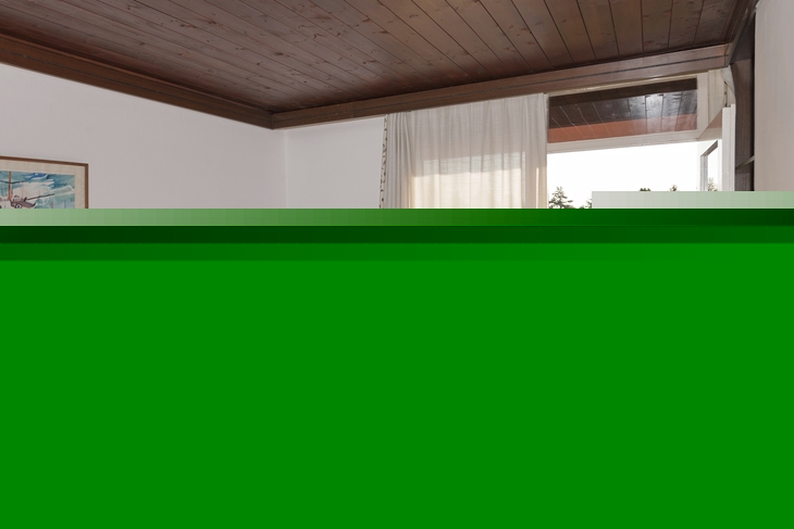Blick aus einem Zimmer mit Bett und geöffneter Tür zur begrünten Terrasse.