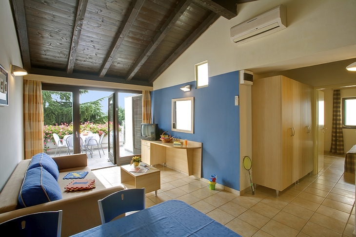 Innenraum einer Ferienwohnung mit Sofa, Tisch, TV und Zugang zu einer Terrasse.