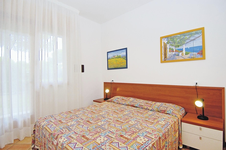 Helles Schlafzimmer mit Doppelbett, farbigem Bettbezug und zwei Nachttischlampen.