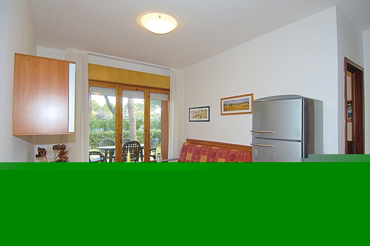 Essbereich mit gedecktem Tisch, Kühlschrank, Sofa und Blick auf Terrasse und Garten.