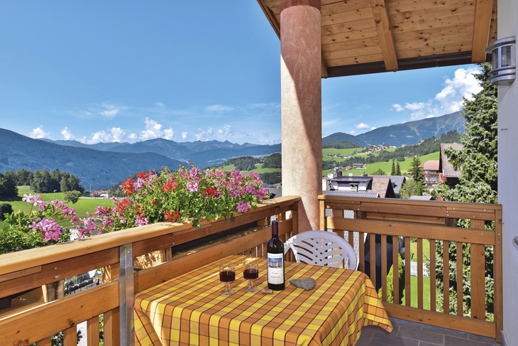 Ausblick von einem Balkon auf Berge und Landschaft bei blauem Himmel.