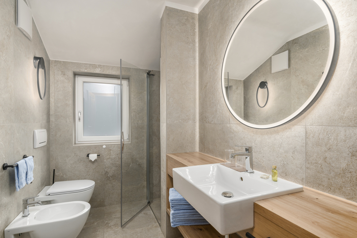 Modernes Badezimmer mit Waschbecken, Dusche und großem rundem Spiegel.