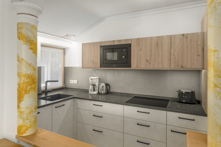 Moderne Küche mit Holzschränken, Mikrowelle, Kaffeemaschine und Wasserkocher.