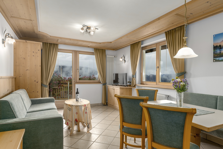 Wohnzimmer mit Sofa, Esstisch, großen Fenstern und Vorhängen in einem Apartment.