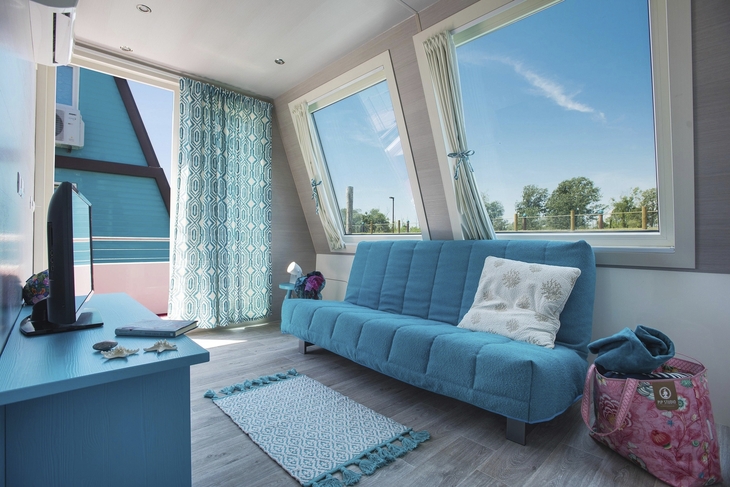 Wohnbereich mit türkisblauem Sofa, großem Fenster und moderner Einrichtung.