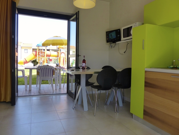 Wohnbereich mit Tisch und Stühlen, Blick auf Terrasse mit Spielplatz draußen.