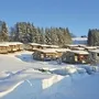 Verschneite Hüttenlandschaft in Scheidegg mit schneebedeckten Bäumen bei klarem Himmel.