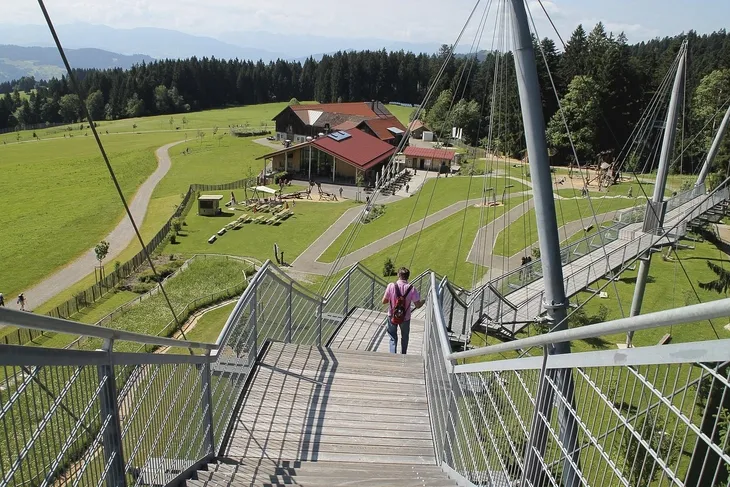 Person geht über Skywalk in Scheidegg mit Blick auf Wiesen und Gebäude.