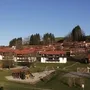 Blick auf einen Spielplatz vor Wohnhäusern mit rotem Dach in einer grünen Landschaft.