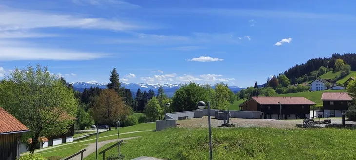 Landschaft mit Wiesen, Bäumen und Bergen im Hintergrund bei klarem Himmel.
