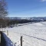 Verschneite Landschaft mit Bauernhof und Bergen im Hintergrund.