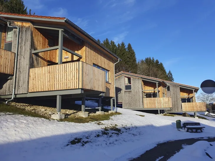Mehrere Holzhäuser in winterlicher Schneelandschaft bei blauem Himmel.